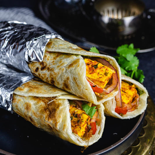 Stack of vegetable wraps on a dark plate with a lime wedge and cilantro.